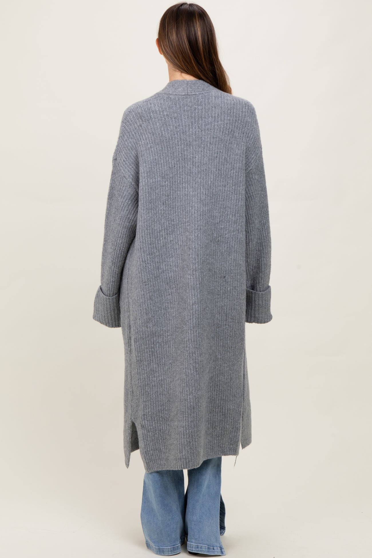 woman wearing a long grey maternity cardigan with ribbed texture and side slits, viewed from the back