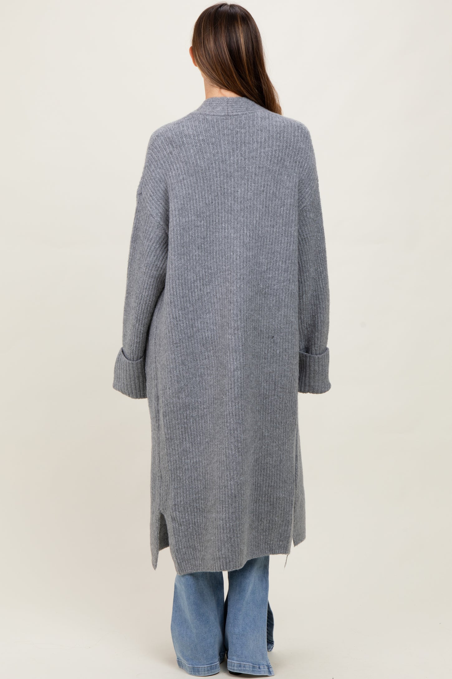 woman wearing a long grey maternity cardigan with ribbed texture and side slits, viewed from the back