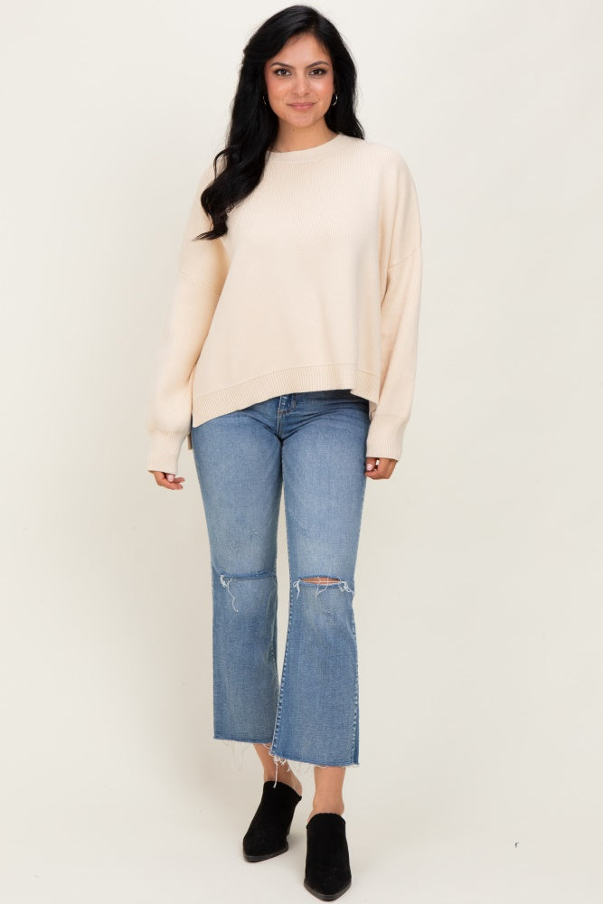 woman wearing a cream oversized knit sweater with distressed light blue cropped jeans and black ankle boots