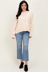 woman wearing a cream oversized knit sweater with distressed light blue cropped jeans and black ankle boots