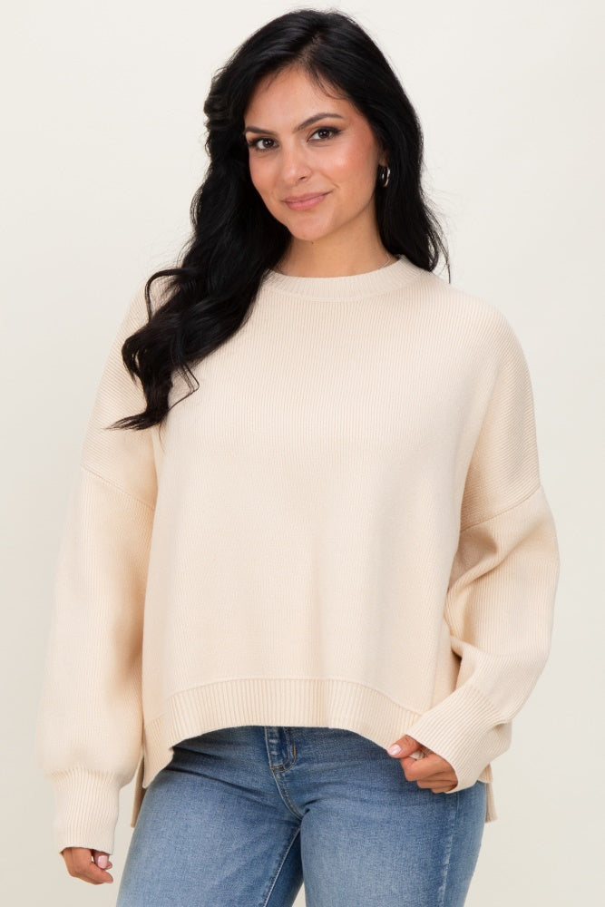 woman wearing a cream oversized sweater with ribbed texture and side slits, paired with blue jeans