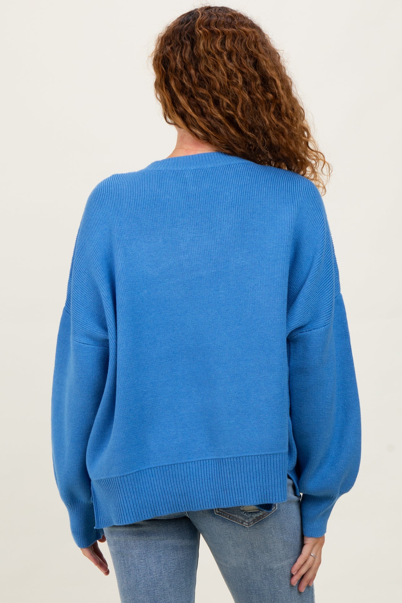 woman wearing a loose-fitting blue sweater with balloon sleeves and a ribbed hem, seen from the back