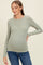 woman wearing a light green long sleeve maternity top and showing her baby bump while smiling