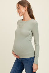 woman wearing a light green long sleeve maternity top and showcasing her baby bump while smiling
