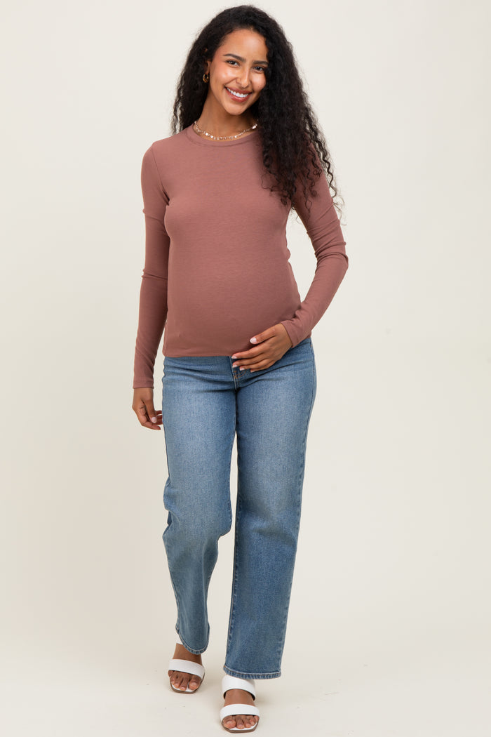 woman wearing a rust ribbed long sleeve maternity top and blue straight leg jeans, holding her baby bump