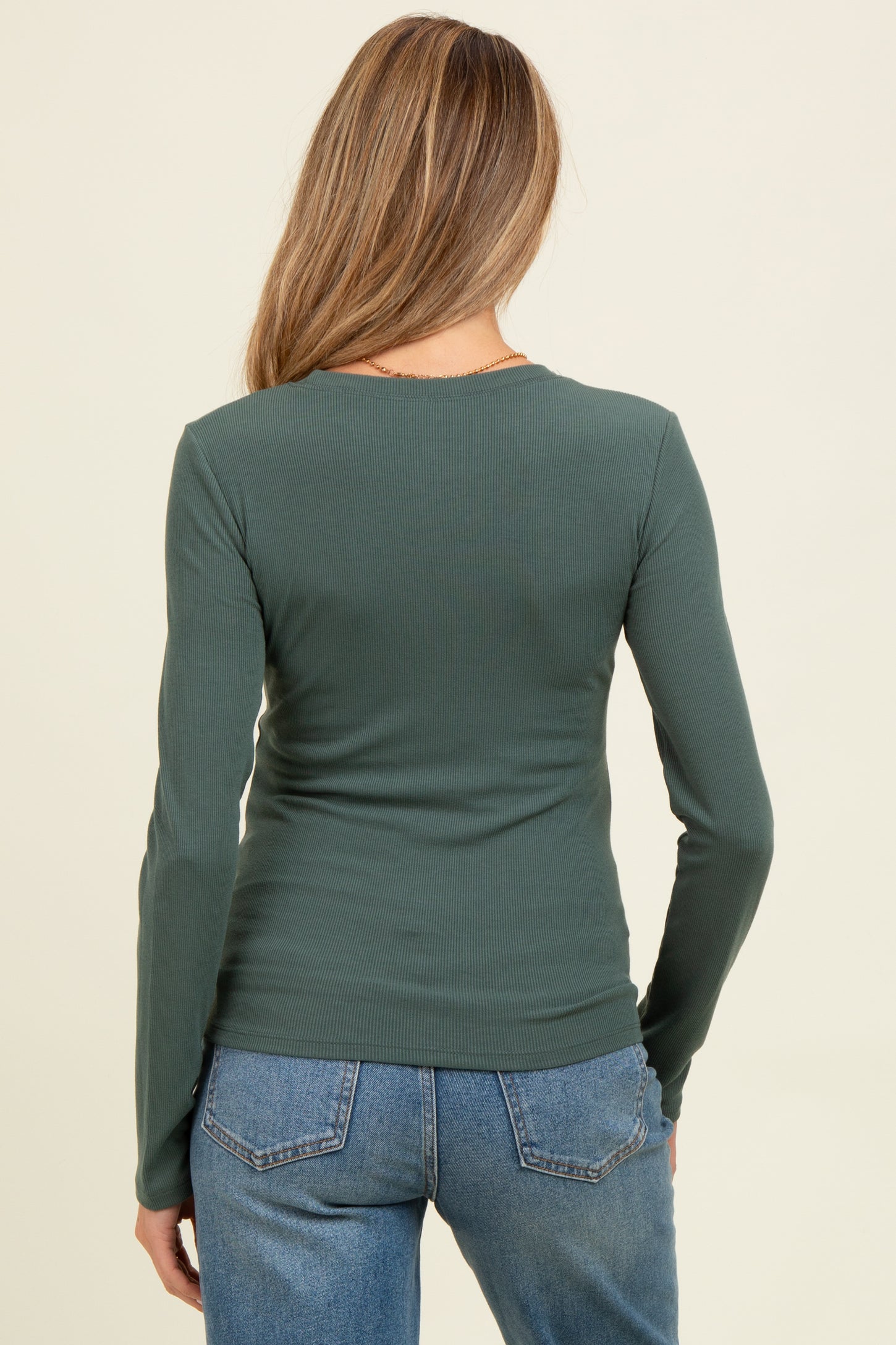 woman wearing a green long sleeve maternity top, viewed from the back, paired with blue jeans