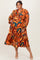 woman wearing an orange and blue floral print plus-size dress with long sleeves and a tiered skirt, smiling at the camera