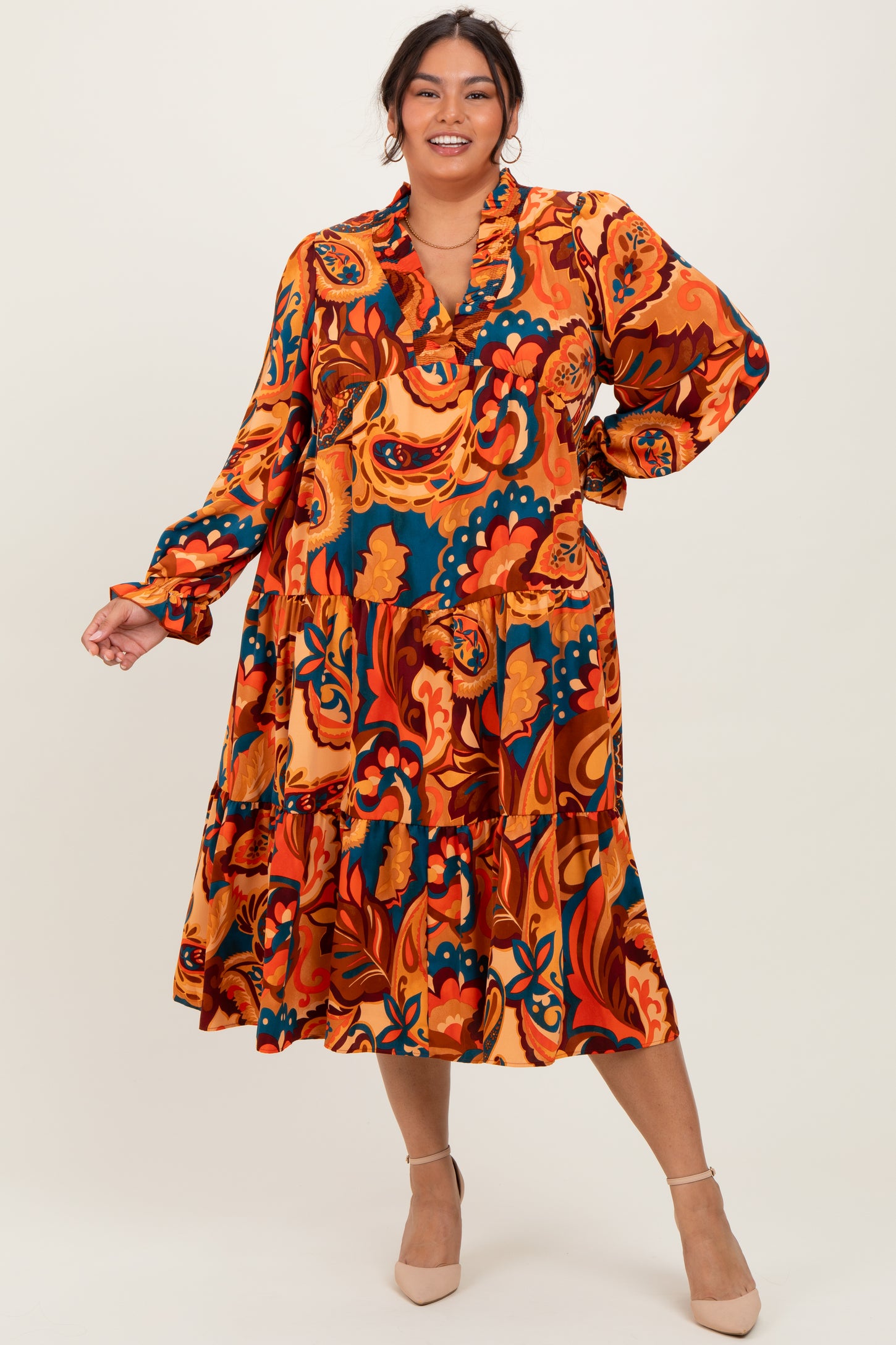 woman wearing a vibrant orange floral plus size dress with long sleeves and a tiered skirt, standing against a neutral background