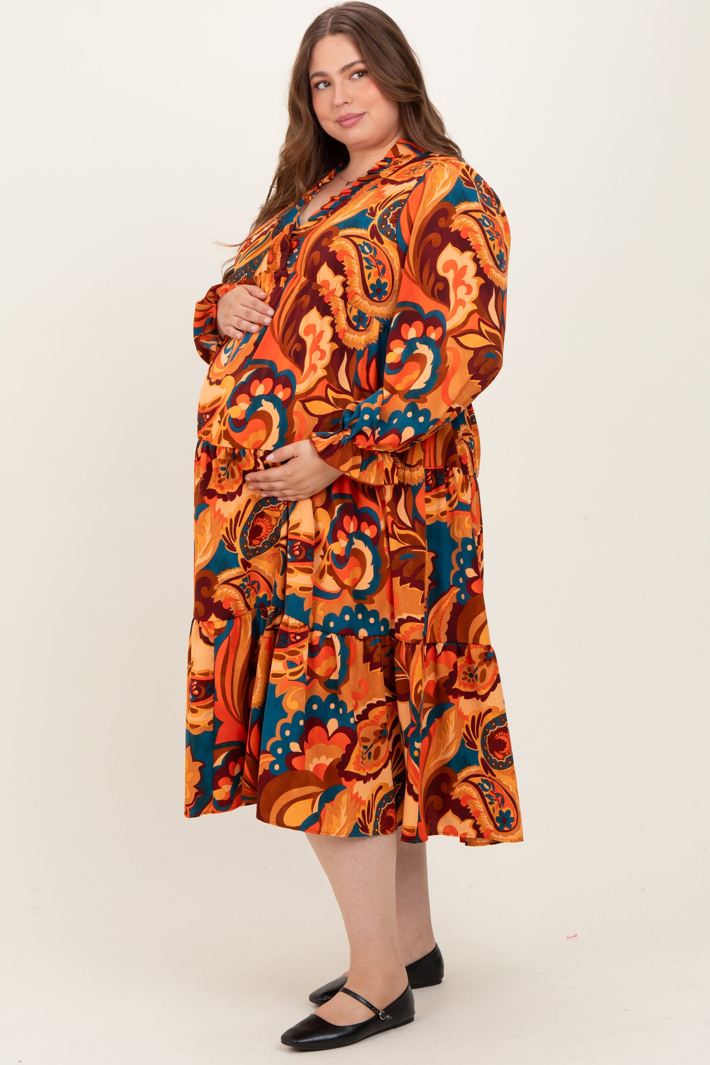 woman wearing a colorful floral maternity dress with long sleeves and a flowing skirt, showcasing her baby bump