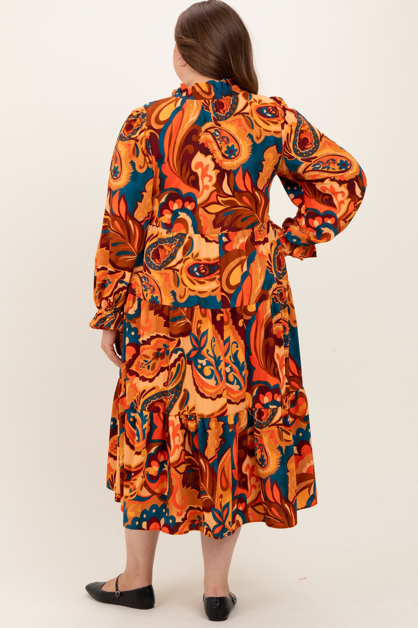 woman wearing a multicolored paisley print maternity dress with long sleeves and ruffled hemline, showing a baby bump from the back