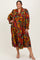 woman in a colorful floral print plus size dress with long sleeves and a tiered skirt, standing and smiling