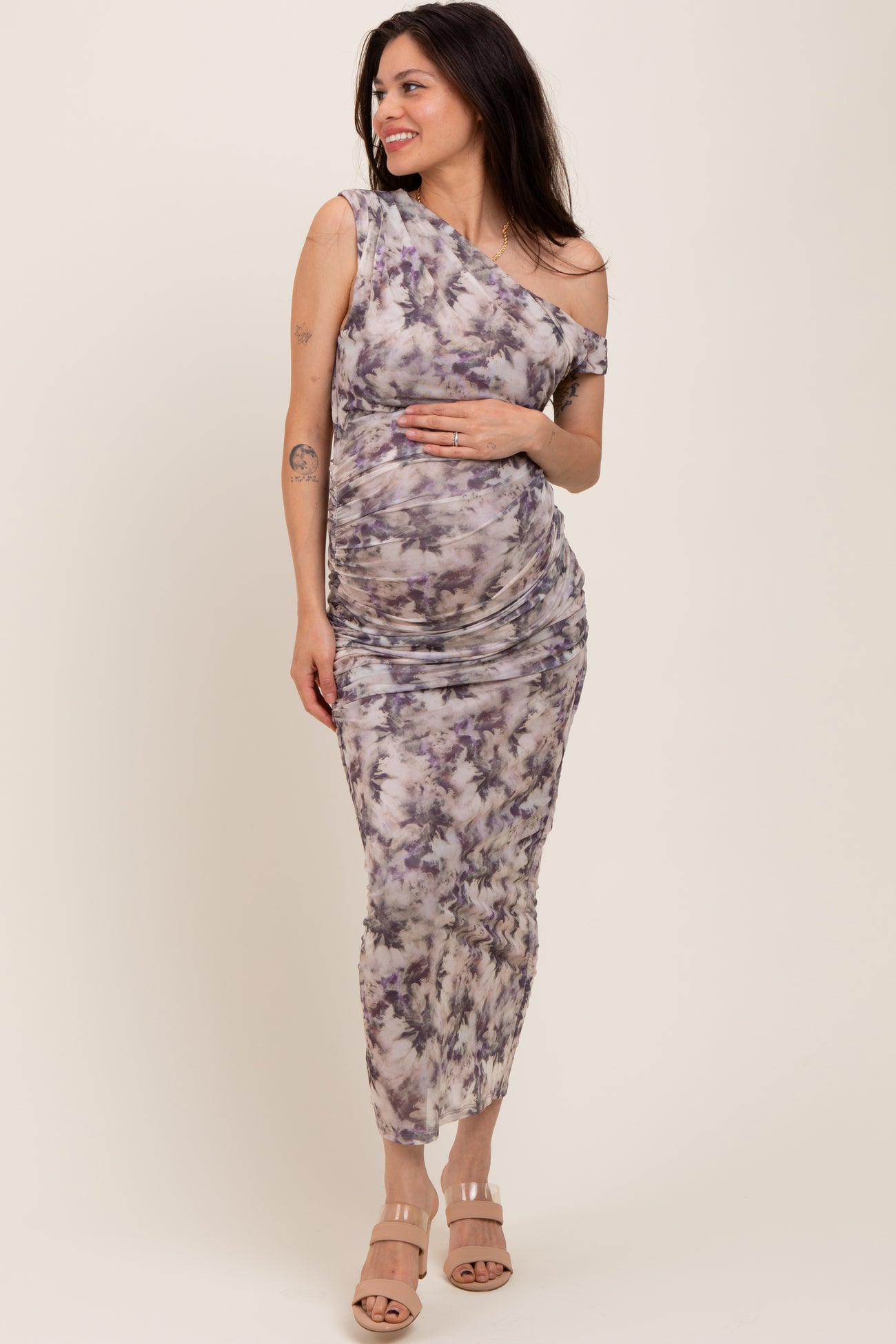 woman wearing a purple tie-dye one-shoulder maternity dress and holding her baby bump