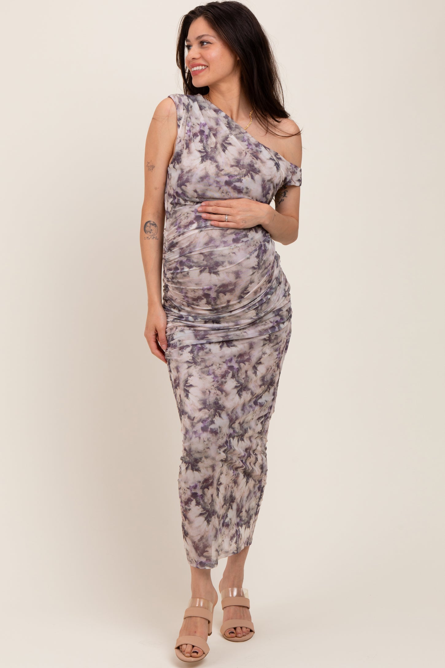 woman wearing a purple tie-dye one-shoulder maternity dress and holding her baby bump