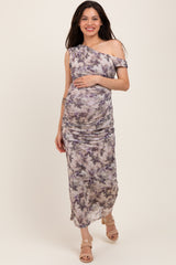 woman wearing a purple and gray tie-dye one-shoulder maternity dress and holding her baby bump