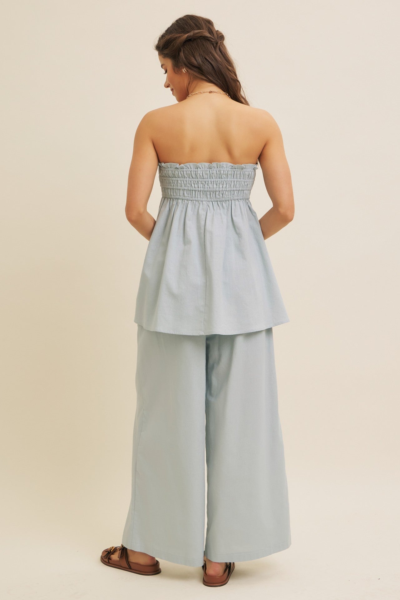 woman wearing a light blue strapless peplum top with smocked bodice and wide-leg pants, view from the back
