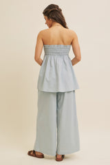woman wearing a light blue strapless peplum top with smocked bodice and wide-leg pants, view from the back