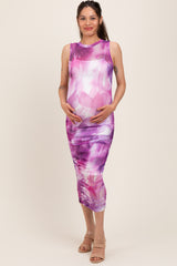 woman wearing a sleeveless purple and pink print maternity dress with gathered detailing and holding her baby bump