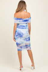 woman wearing a floral off-the-shoulder maternity dress in blue tones, showing a fitted silhouette and sheer layers