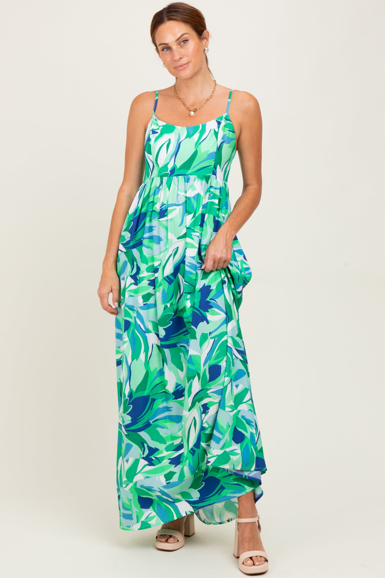 woman wearing a green and blue leaf print maxi dress with adjustable straps and flowy silhouette
