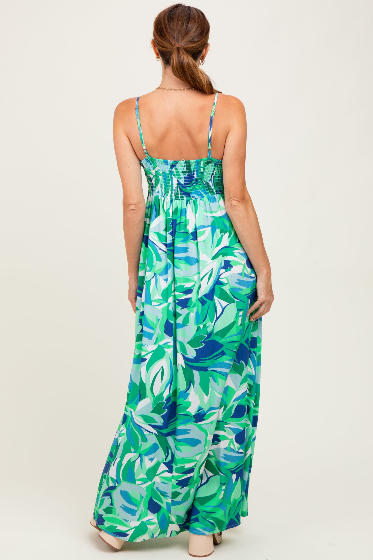 woman wearing a green floral maxi dress with adjustable straps and a smocked back, seen from the back