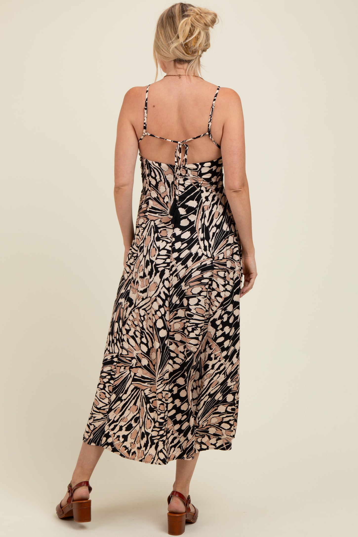 woman wearing a black and tan floral print maternity maxi dress with adjustable straps and a tied back detail