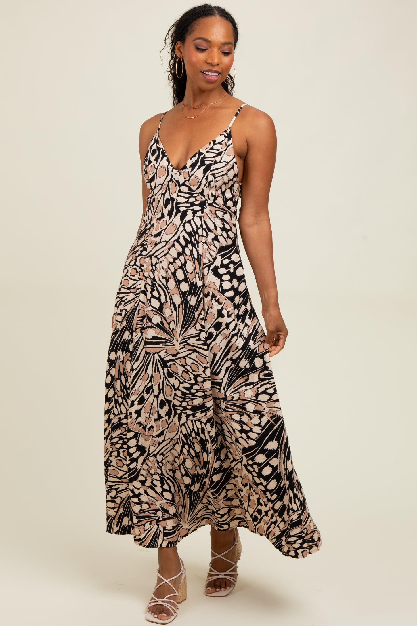 woman wearing a spaghetti strap maxi dress with a black and beige leaf print and stylish shoes