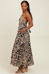 woman wearing a black and beige floral maxi dress with spaghetti straps and side pockets, model posing sideways