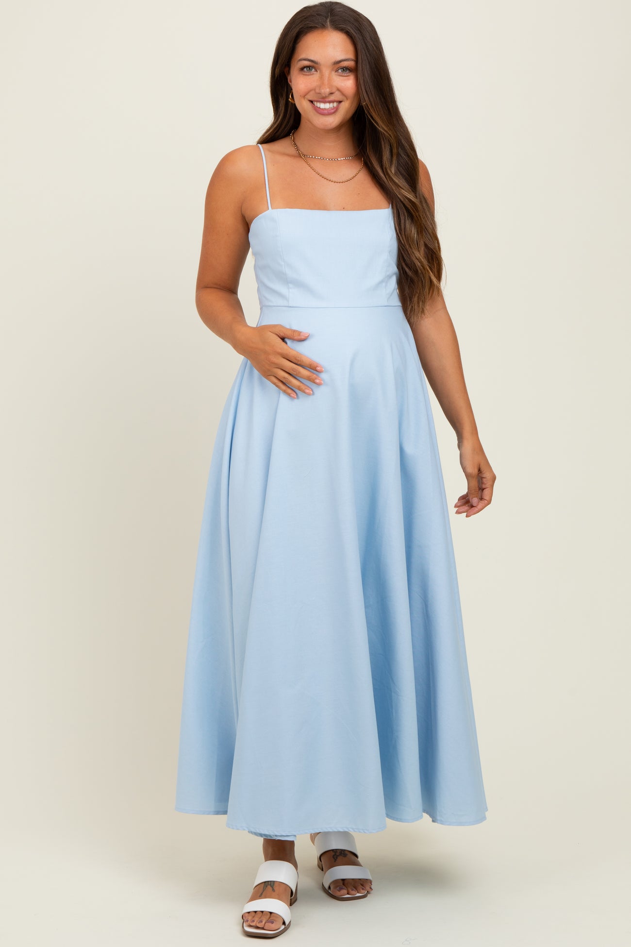woman wearing a light blue maternity maxi dress with spaghetti straps and holding her baby bump