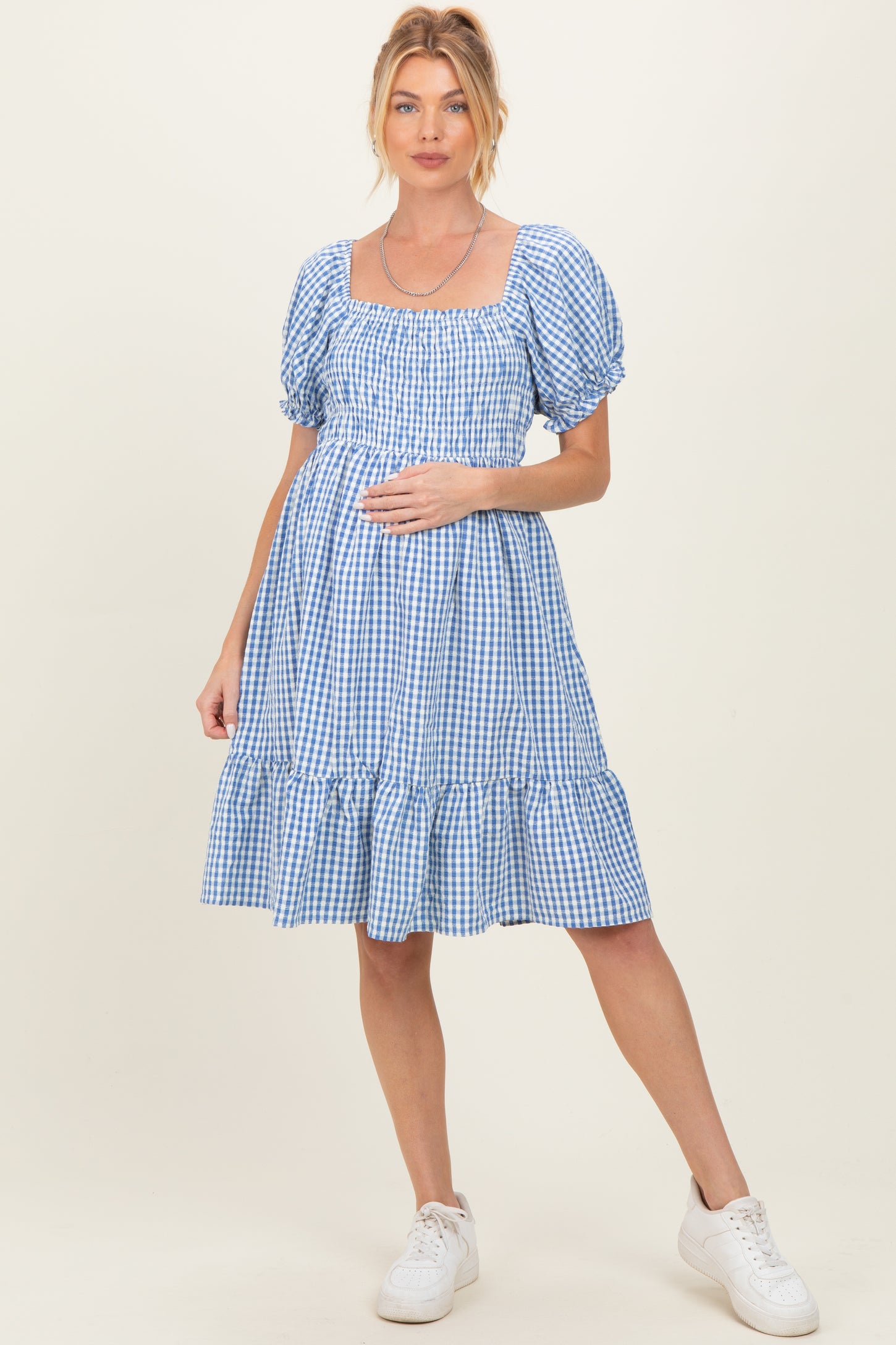 woman wearing a blue and white gingham maternity dress with puff sleeves and a ruffled hem, holding her baby bump