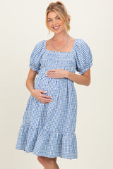 woman wearing a blue and white gingham maternity dress with short puff sleeves and a ruffled hem, showing her baby bump