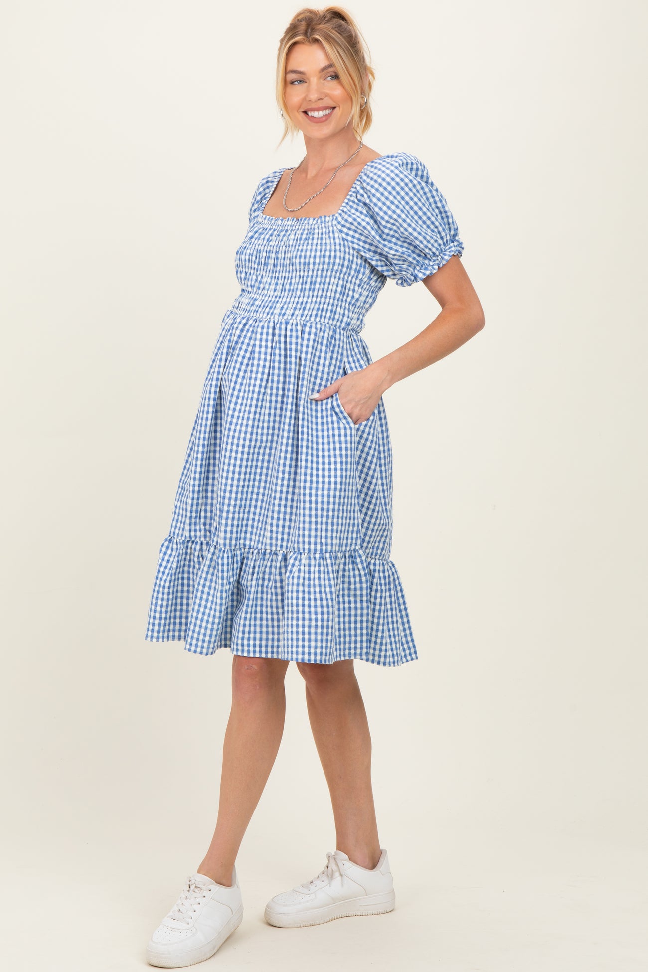 woman wearing a blue gingham maternity dress with puff sleeves and pockets, showing her baby bump