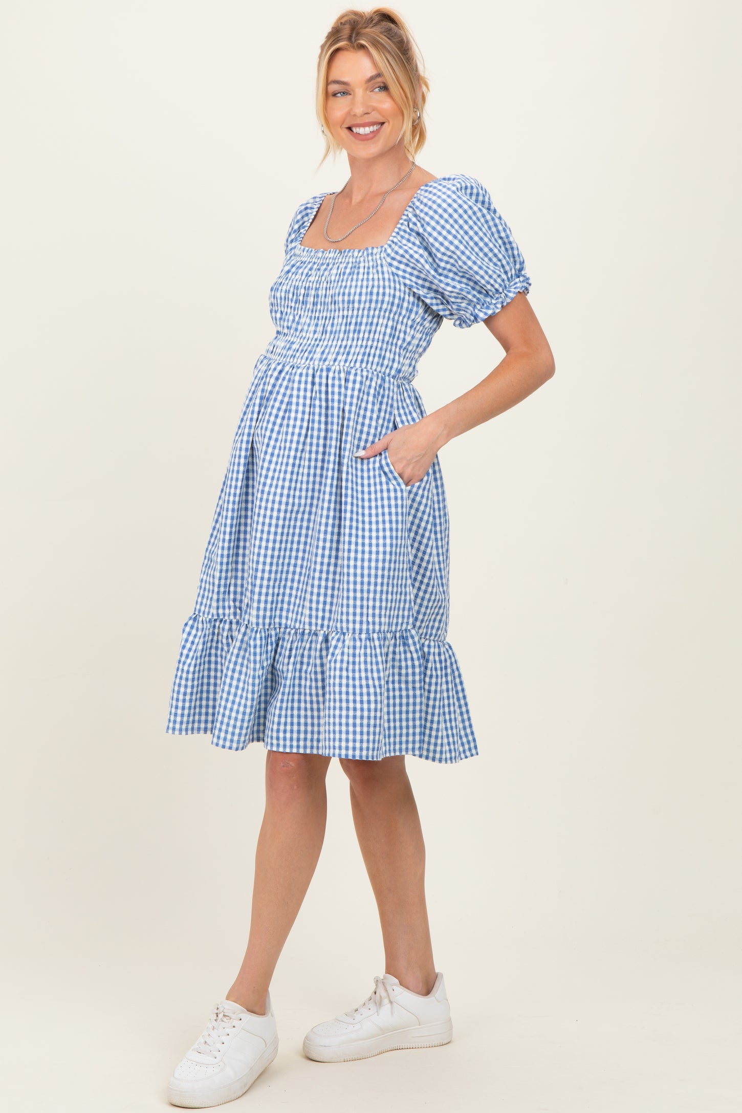 woman wearing a blue gingham maternity dress with puff sleeves and pockets, showing her baby bump