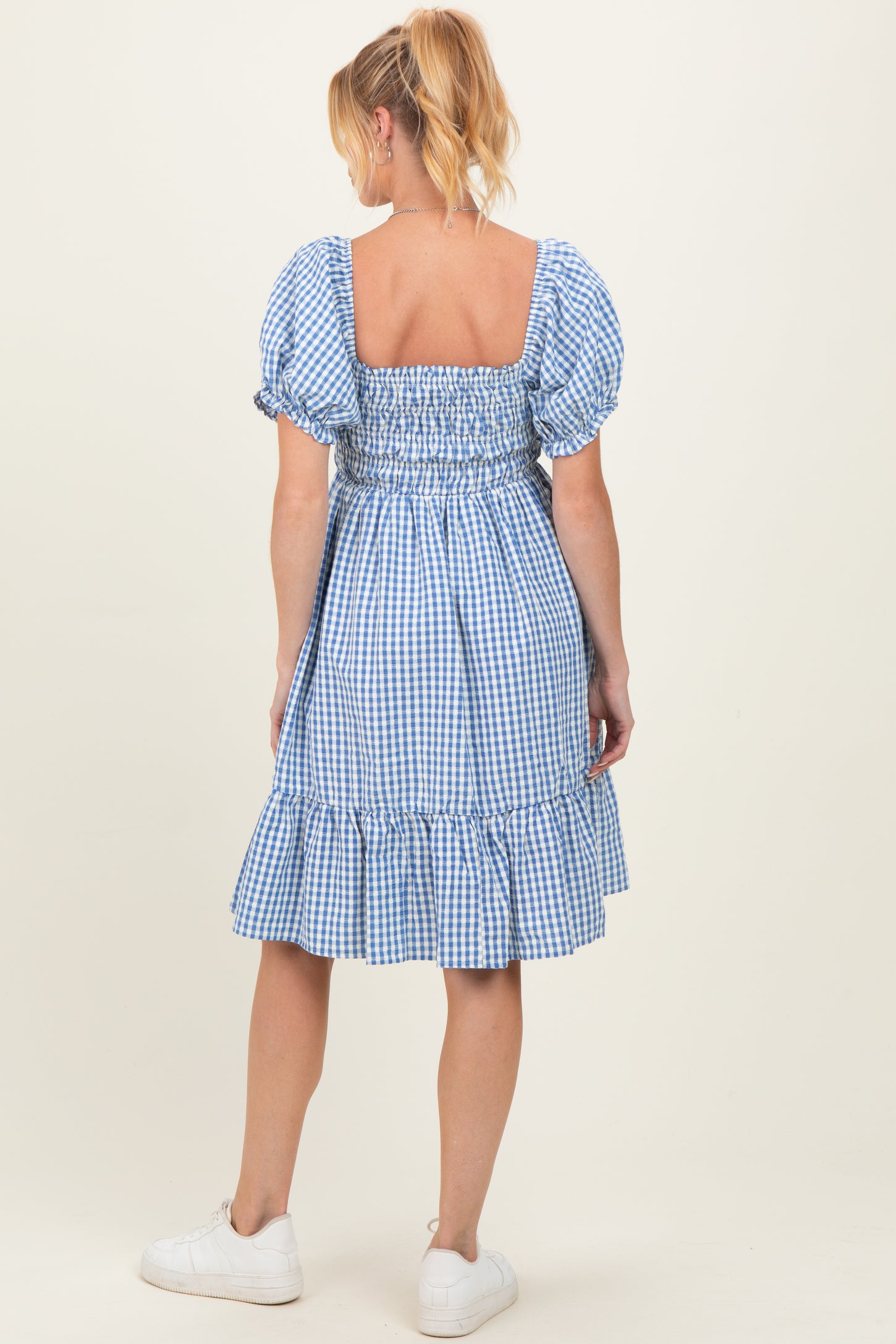 woman wearing a blue gingham maternity dress with puff sleeves and a ruffled hem, showing a baby bump