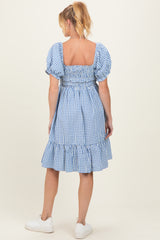 woman wearing a blue gingham maternity dress with puff sleeves and a ruffled hem, showing a baby bump