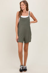 woman wearing an olive green short overalls with a white tank top underneath and black sneakers