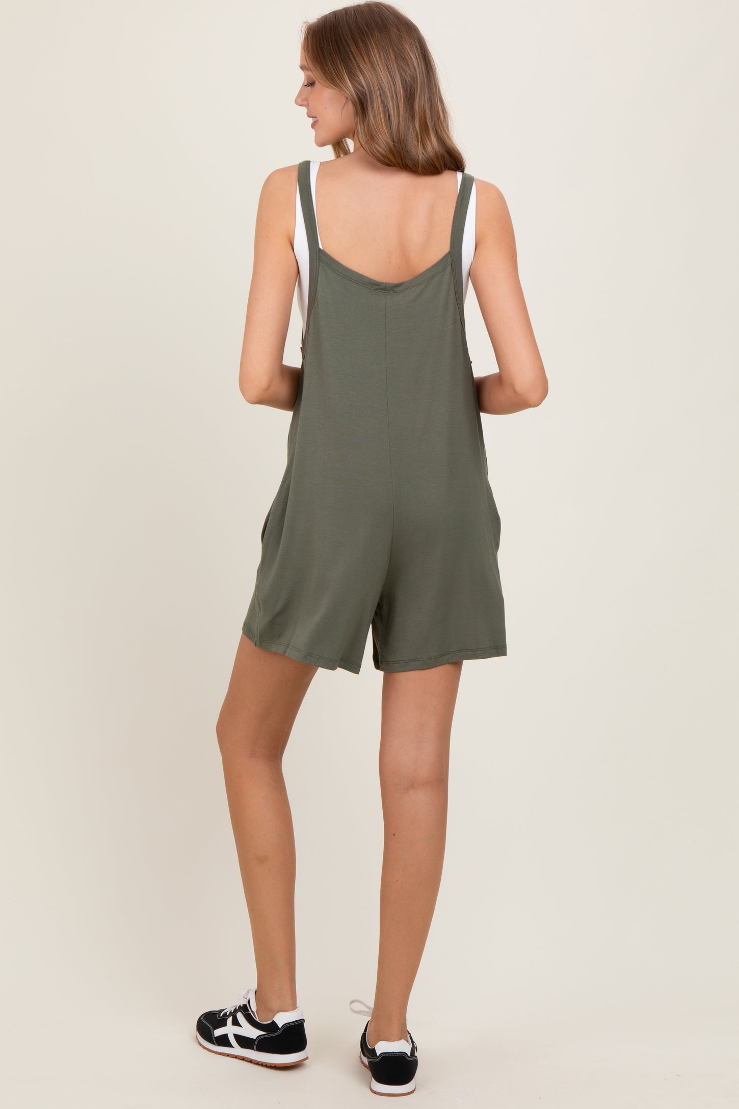 woman wearing a back view of an olive green sleeveless romper with adjustable straps and side pockets