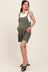 woman wearing a green maternity romper with pockets and a white tank top, showing her baby bump