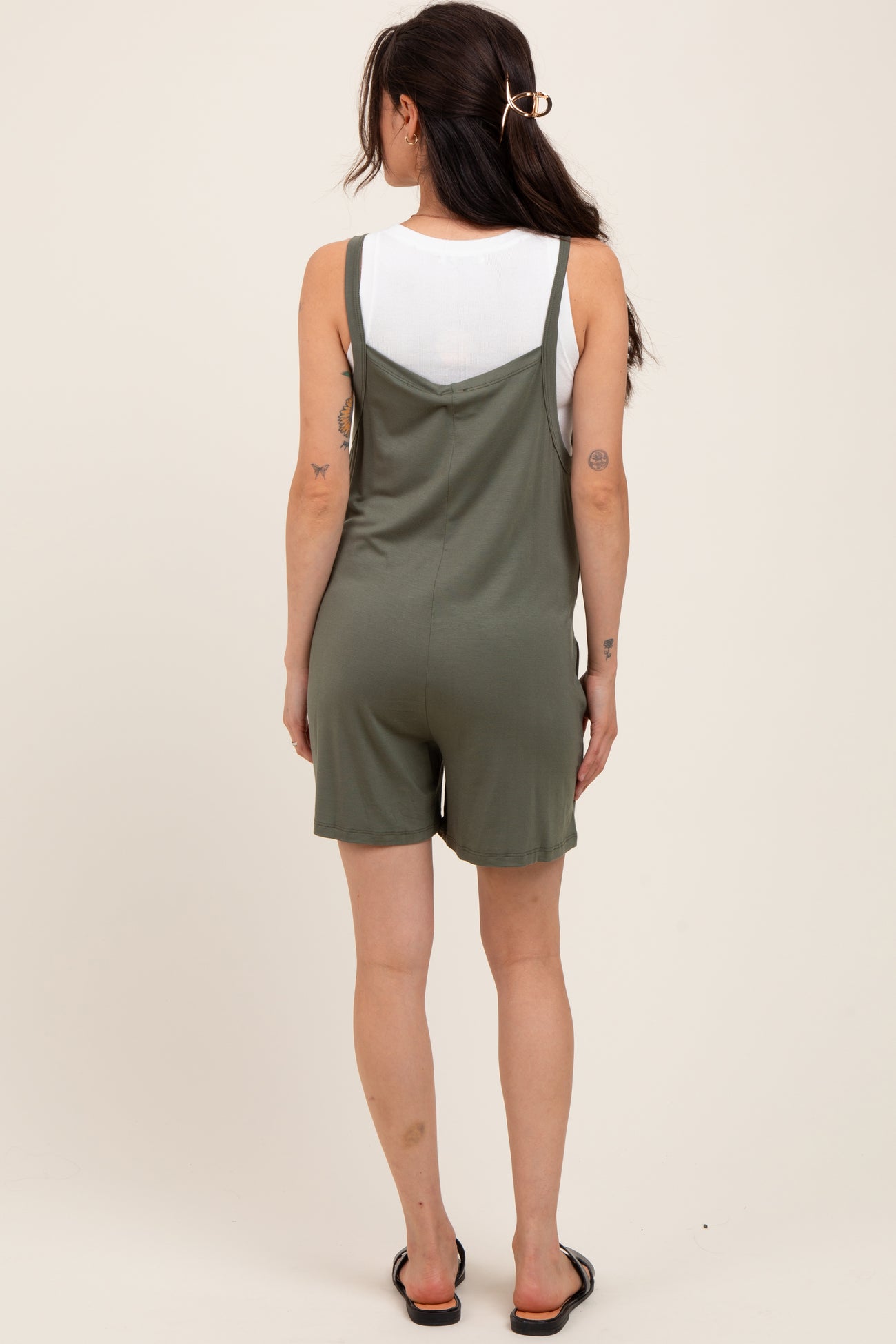 woman wearing a green maternity romper with a relaxed fit and adjustable straps, showing a casual style from the back