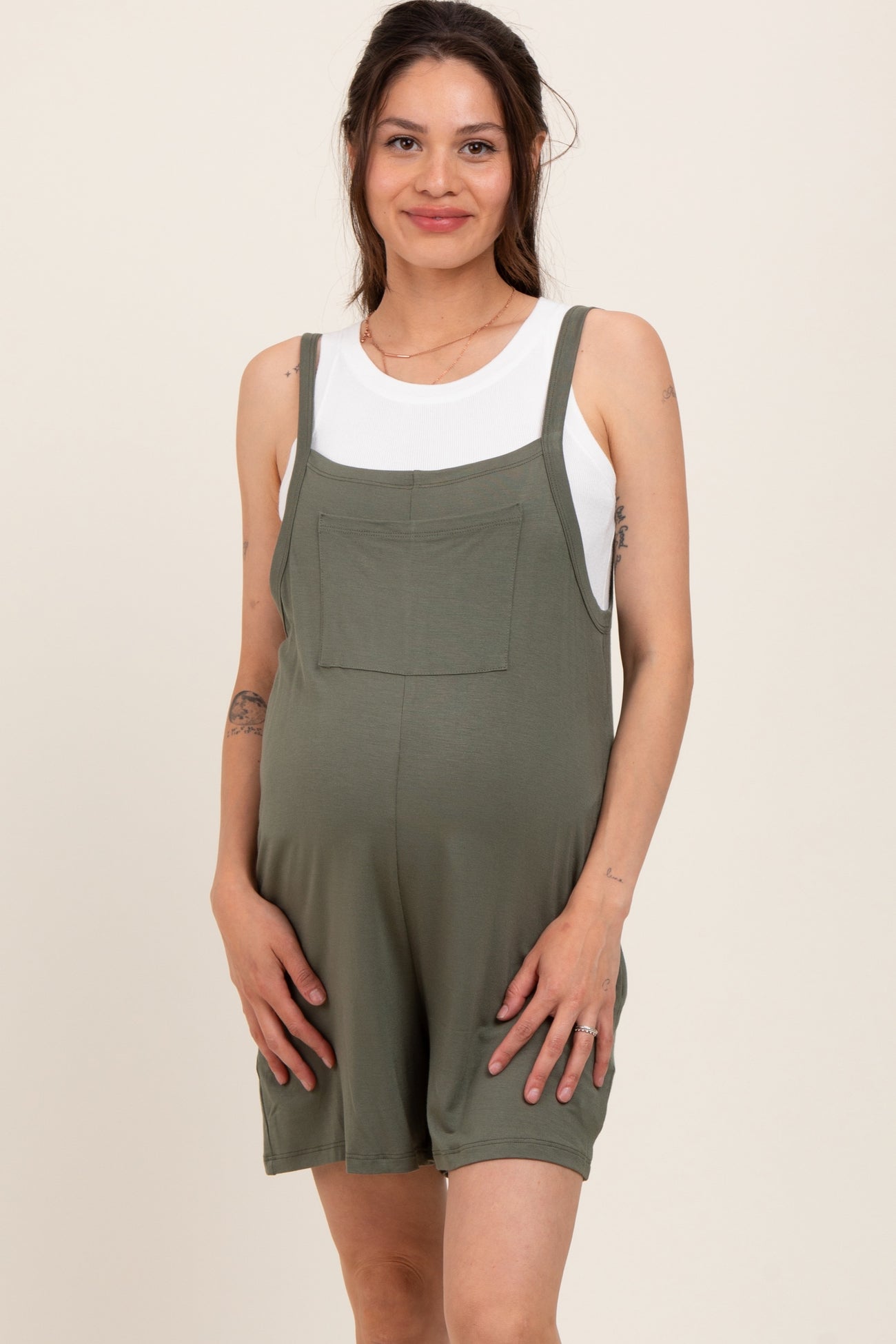woman wearing a green maternity romper with a pocket, showing her baby bump