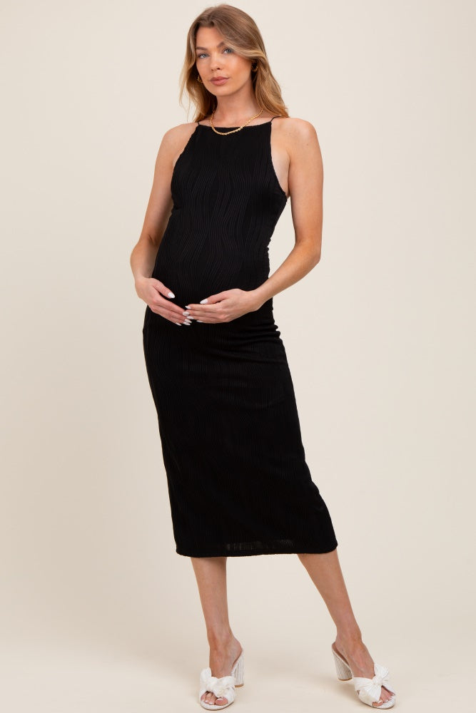 woman wearing a black ribbed maternity dress, holding her baby bump with a relaxed smile