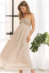 woman wearing a beige strapless maxi dress with a crochet bodice and flowing skirt, standing in a bright room