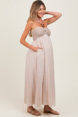 woman wearing a beige strapless maternity maxi dress with a smocked bodice and side pockets, showing her baby bump