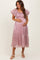 woman wearing a light pink satin maternity dress with puffy sleeves and a tiered skirt, holding her baby bump
