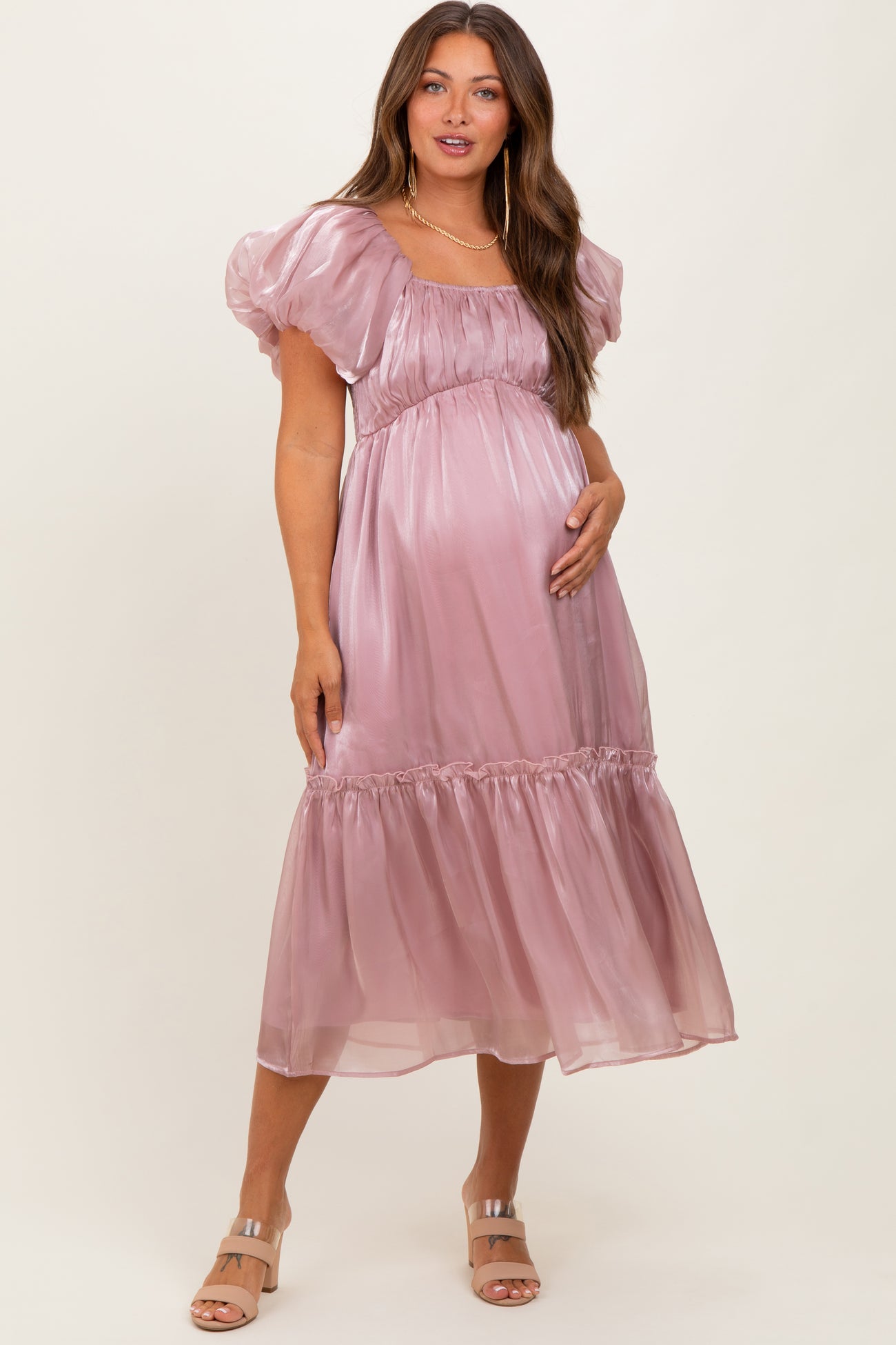 woman wearing a light pink satin maternity dress with puff sleeves and a tiered hem, cradling her baby bump