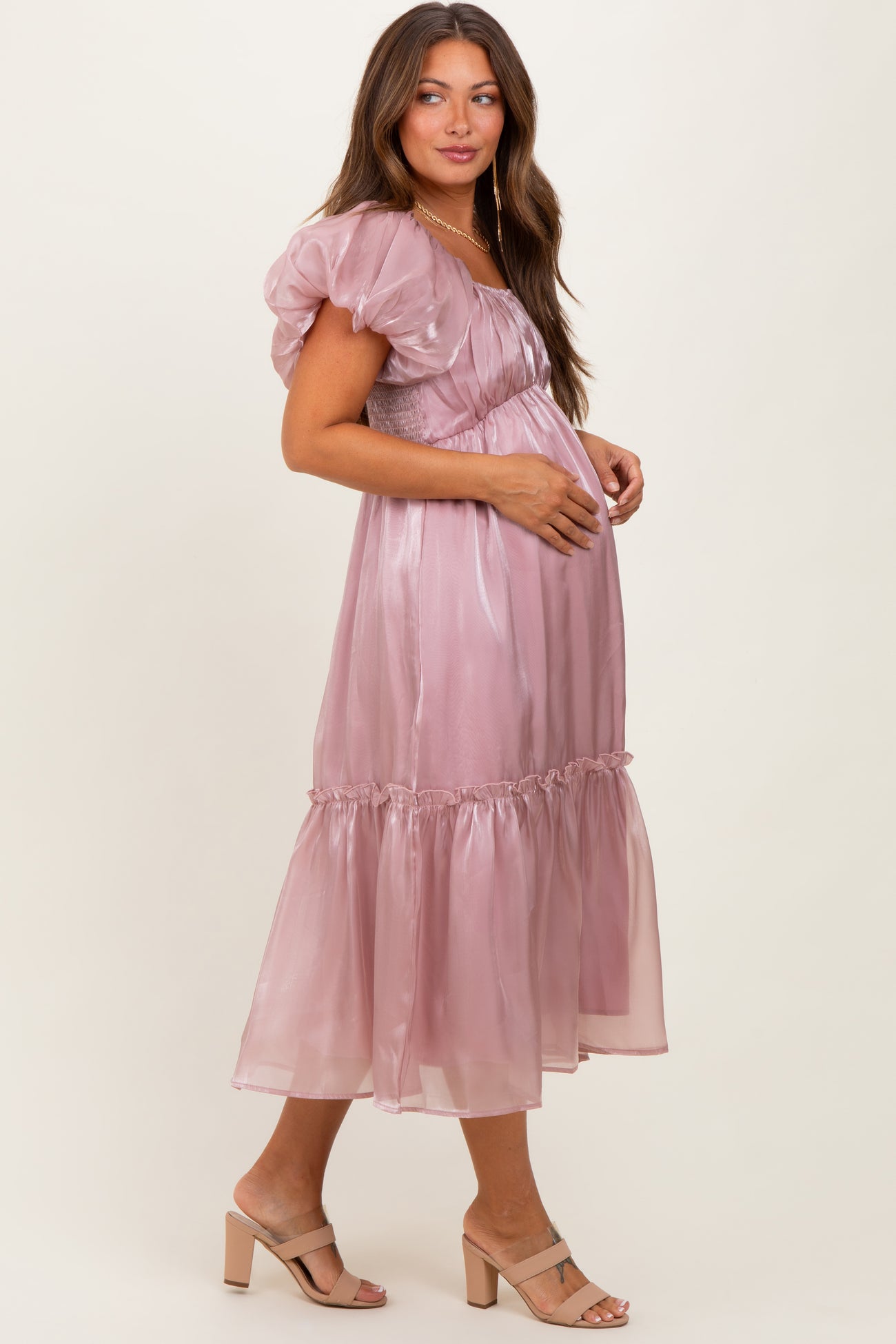 woman wearing a light mauve puff sleeve maternity dress with a ruffled hem and baby bump visible