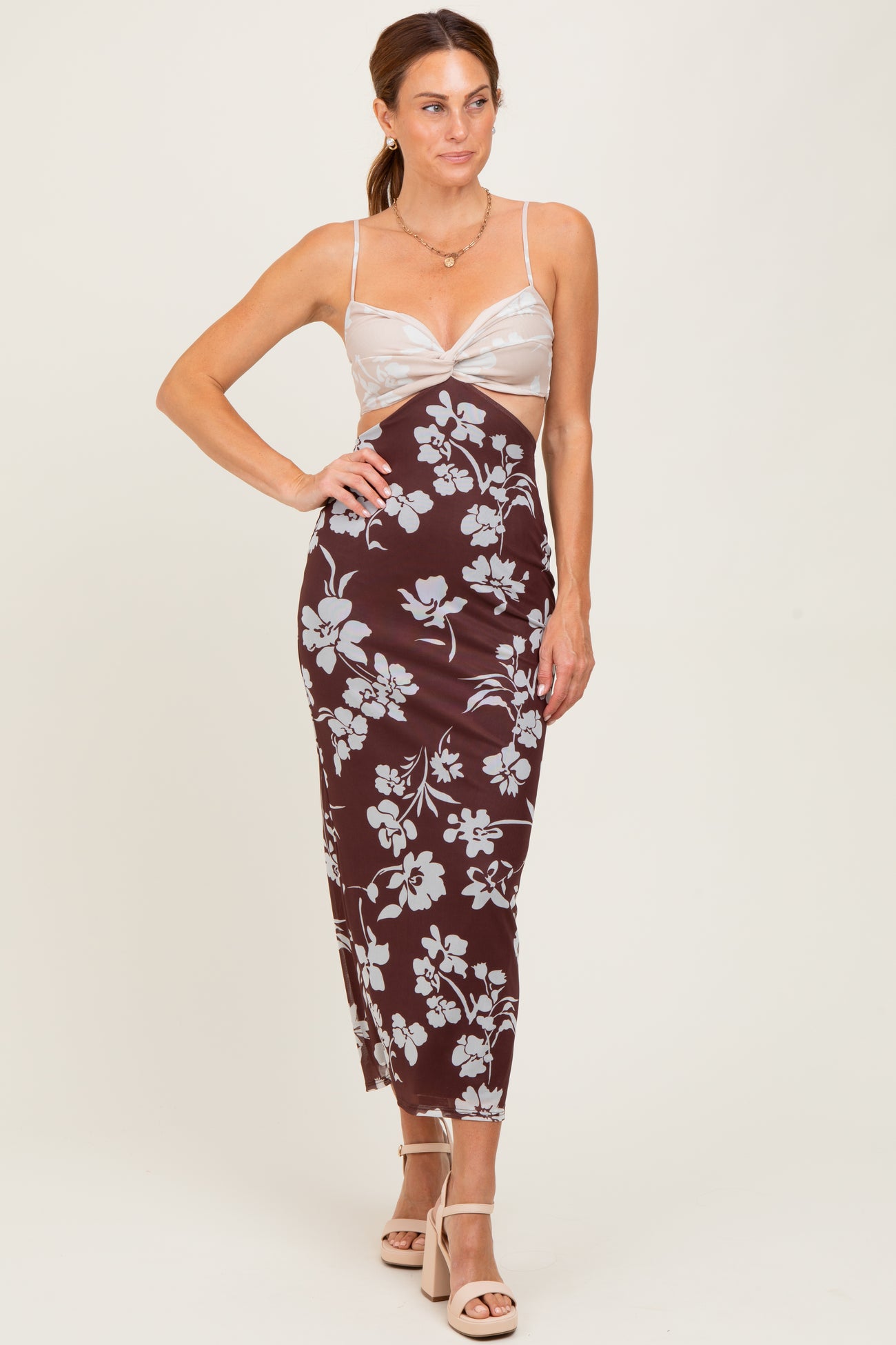 woman wearing a brown floral midi dress with a sheer bodice and spaghetti straps, standing in a neutral background