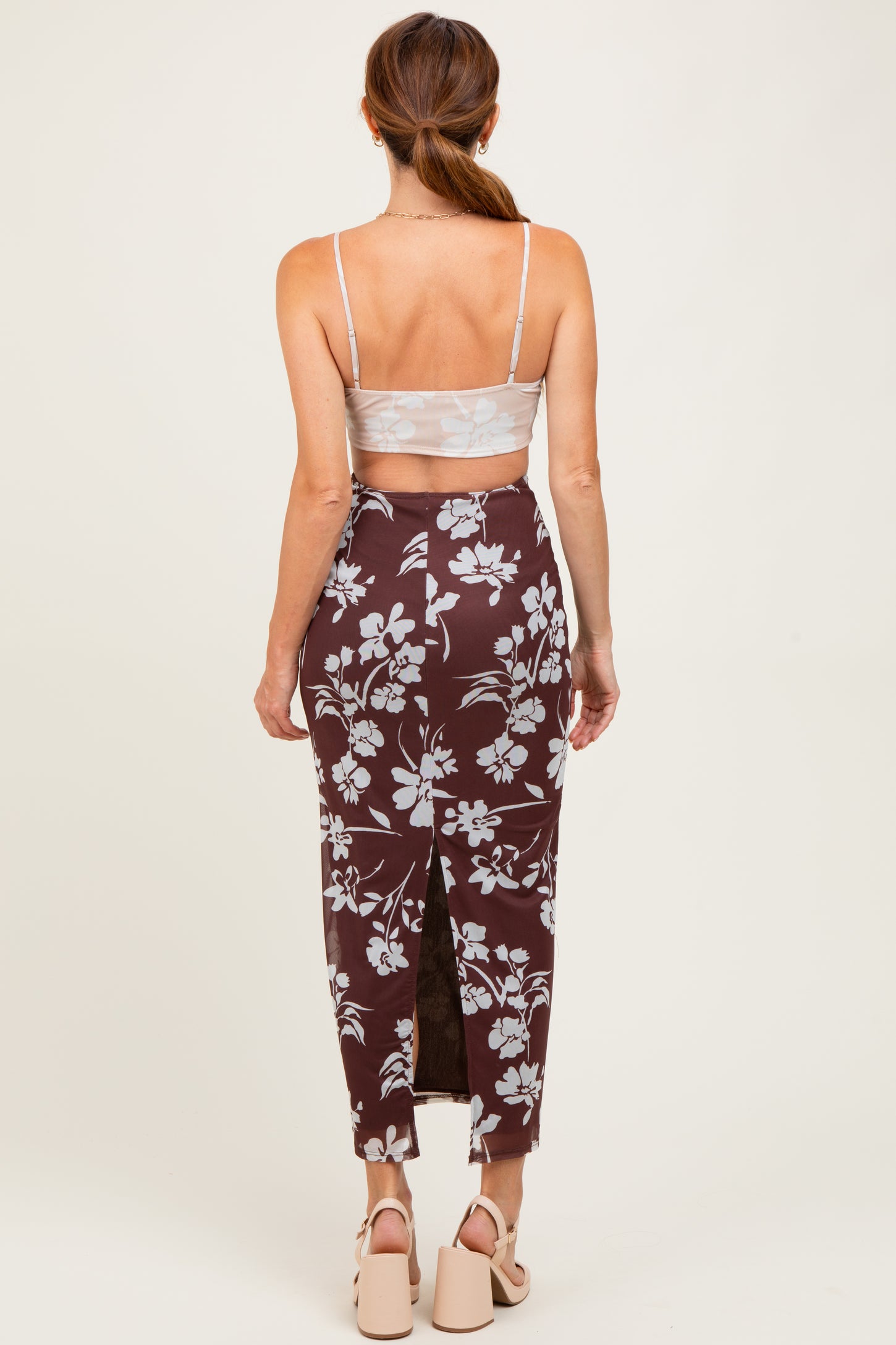 woman wearing a brown floral skirt with a high slit and a light gray crop top, seen from the back