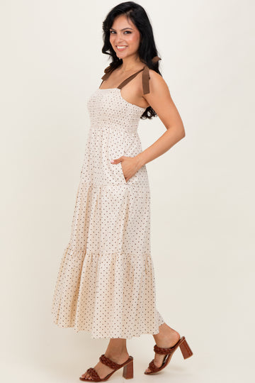 woman wearing a cream polka dot maxi dress with brown straps and pockets, styled with brown heeled sandals