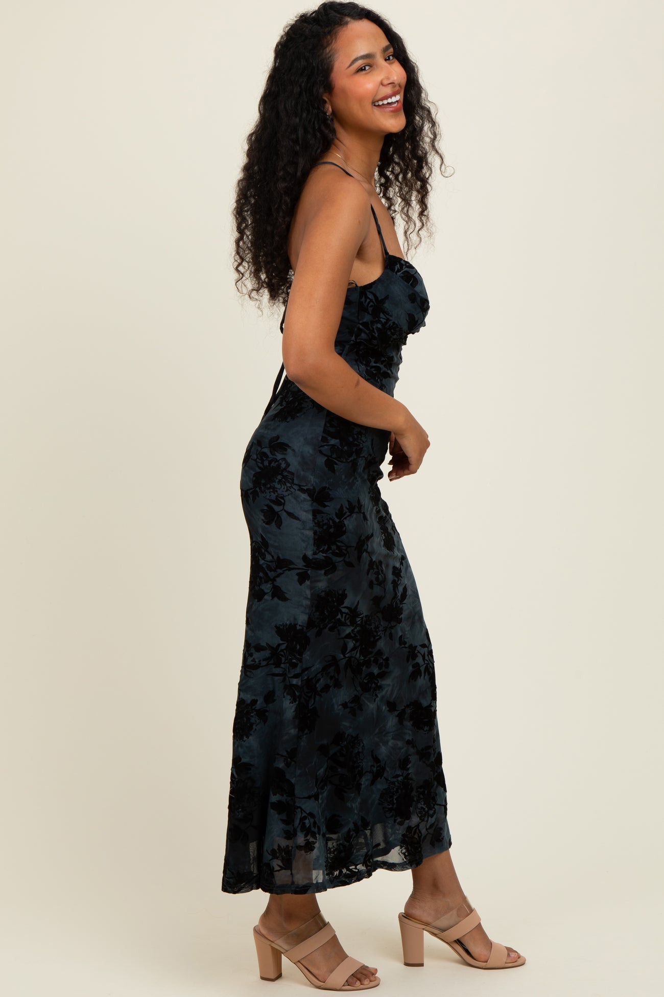 woman wearing a black floral print maxi dress with spaghetti straps and ruffled details, smiling and posing sideways