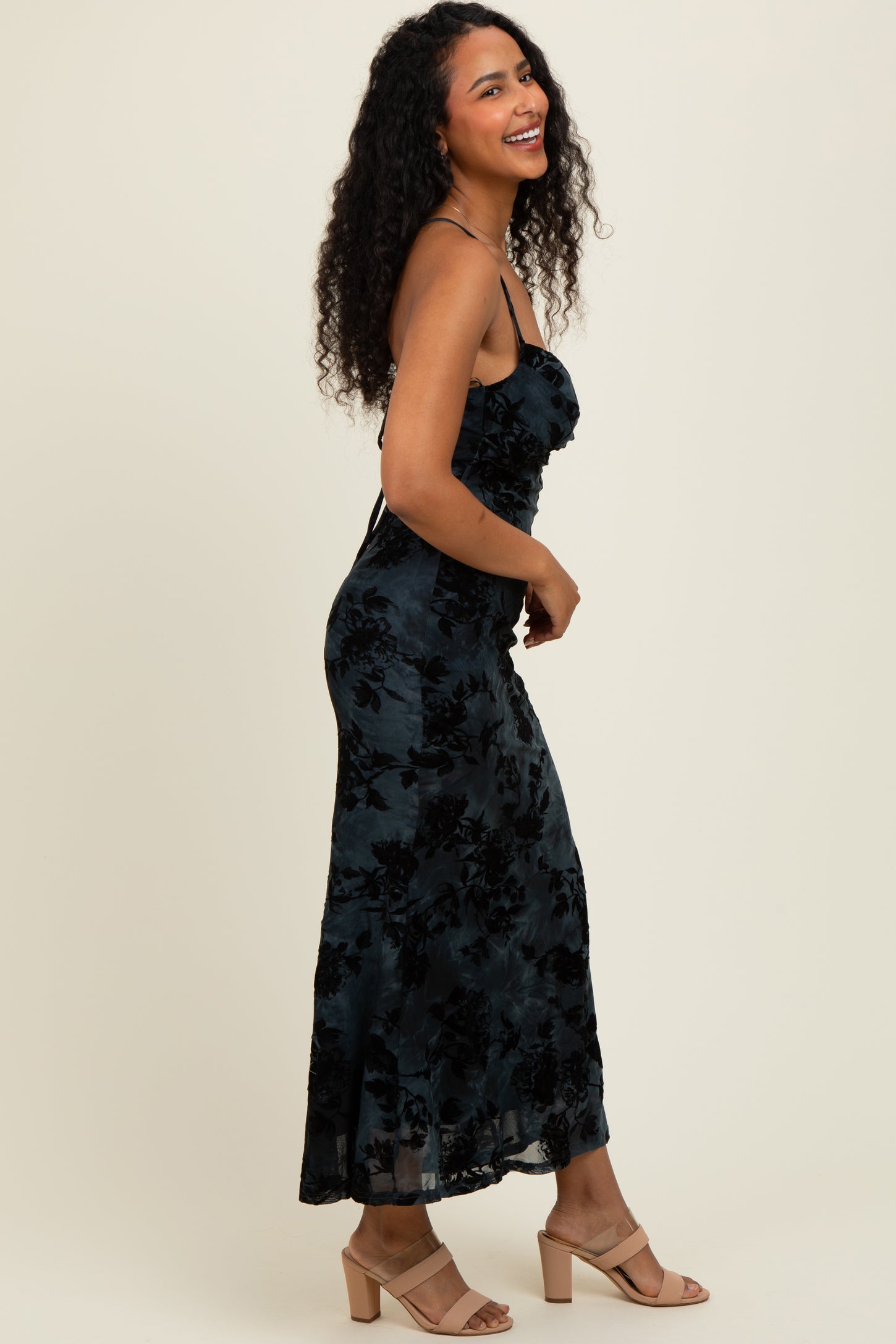 woman wearing a black floral print maxi dress with spaghetti straps and ruffled details, smiling and posing sideways